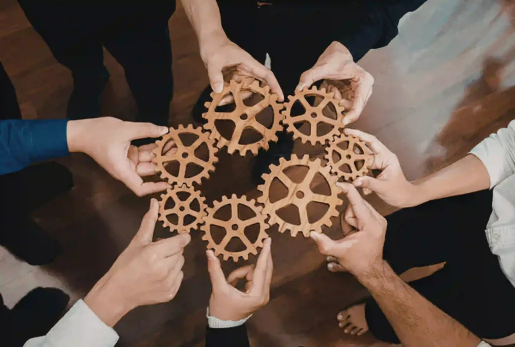 Mehrere Personen halten hölzerne Zahnräder zusammen und symbolisieren Teamarbeit, Zusammenarbeit und abgestimmte Prozesse.